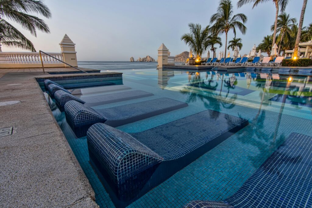 Serene poolside view overlooking the ocean with palm trees and lounge chairs in Cabo San Lucas, capturing tropical tranquility.