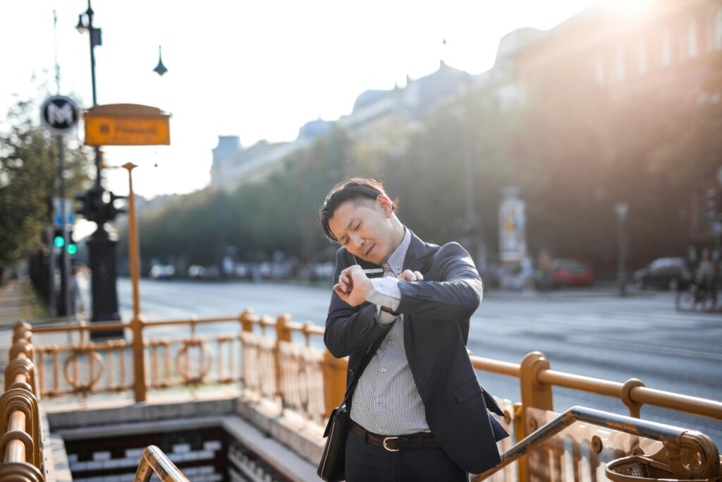 Asian businessman in suit checks time while standing outdoors by city metro entrance