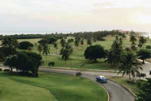 A classic vintage car on a lush Cuban golf course surrounded by palm trees at sunset.